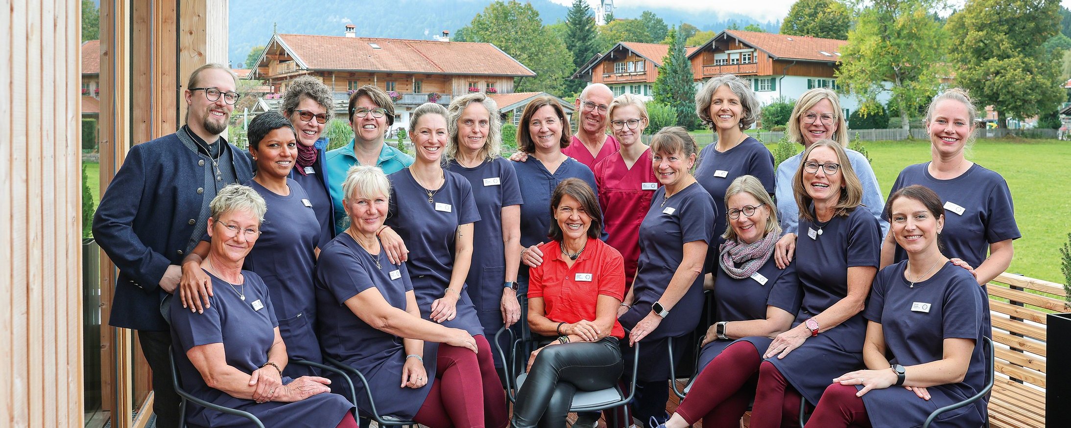 Das Team des Oberland Hospiz steht und sitzt gemeinsam auf einer Holzterrasse vor grüner Landschaft und lächelt in die Kamera.