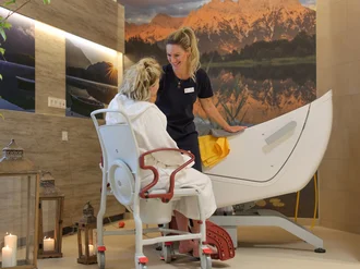 Eine Pflegekraft hilft einer sitzenden Person im barrierefreien Pflegebad des Oberland Hospiz. Kerzen und warmes Licht schaffen eine ruhige Atmosphäre.
