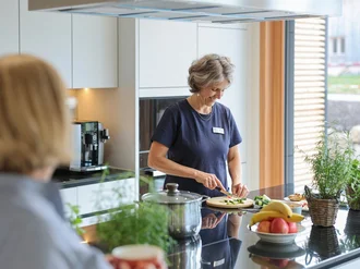 Eine Person bereitet in der hellen Küche des Oberland Hospiz frisches Essen zu, während eine andere Person am Küchentresen steht.