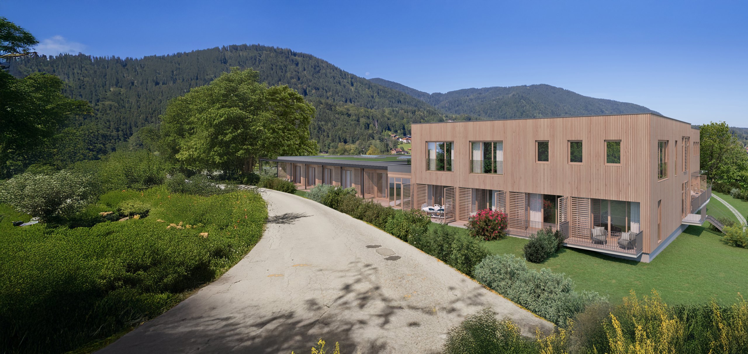 Das moderne Gebäude des Oberland Hospizes liegt inmitten grüner Natur, mit Blick auf bewaldete Berge und blauen Himmel.